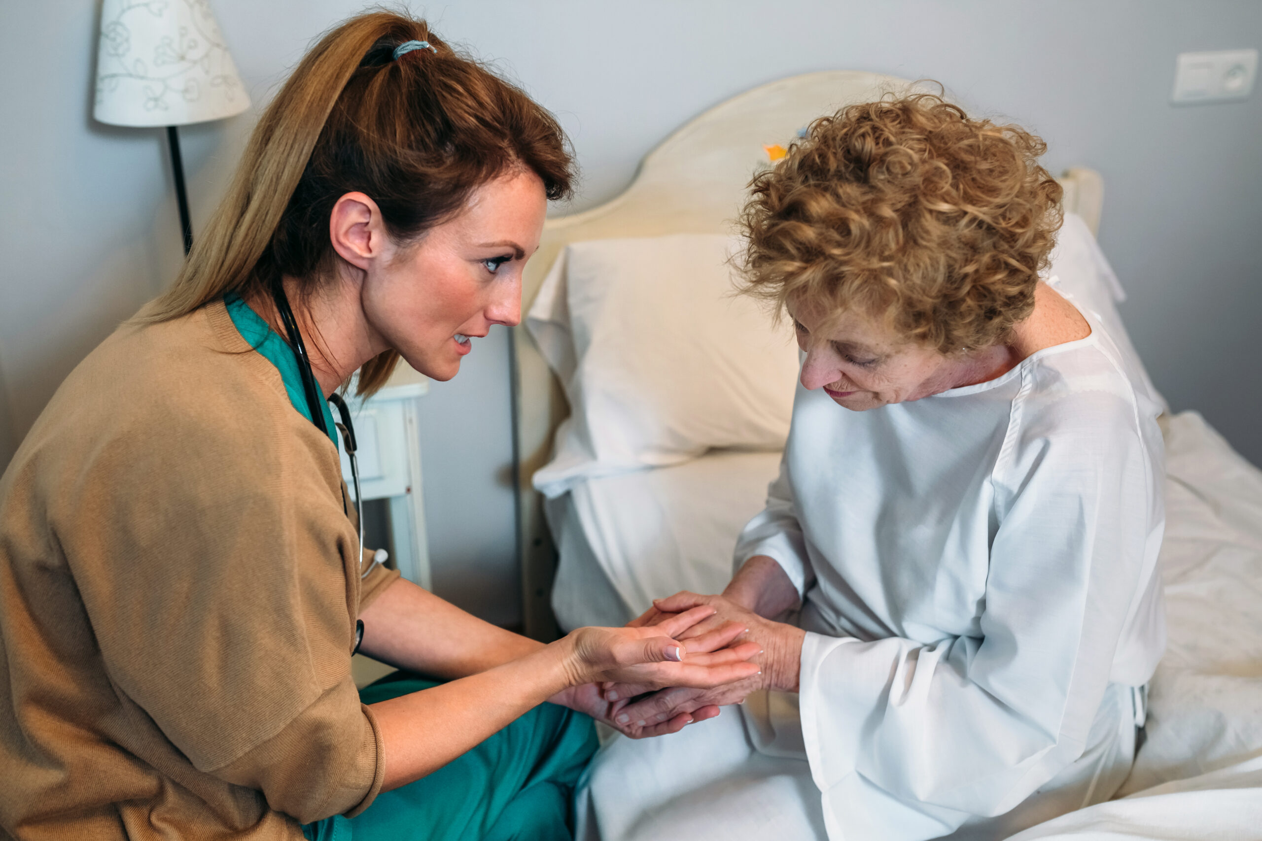 Female doctor giving encouragement to elderly patient by holding her hands