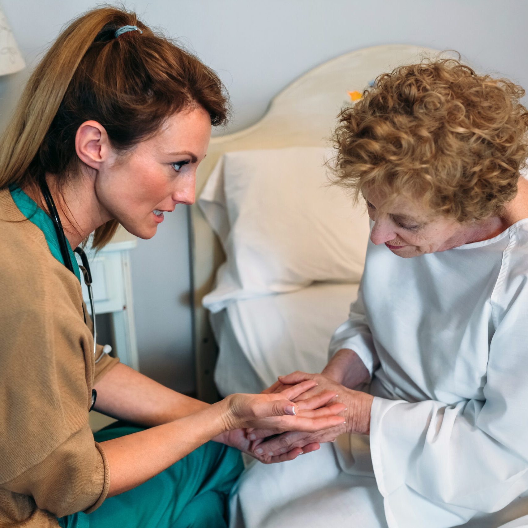 Female doctor giving encouragement to elderly patient by holding her hands